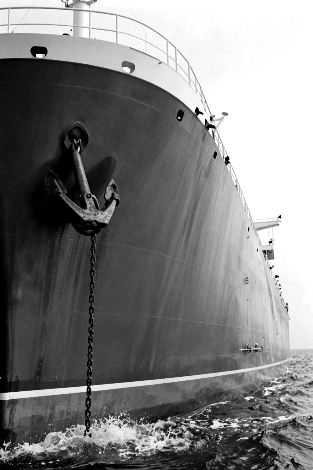 The steel bow of a crude oil tanker with its anchor, spray at the waterline.